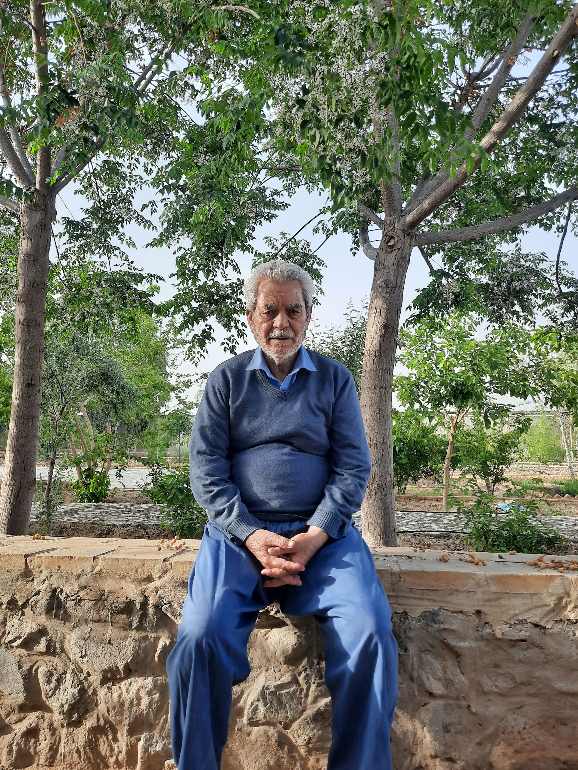 Well-dressed elderly gentleman relaxing in a beautifully maintained garden while a Blue Oyster Concierge professional oversees home watch services.
