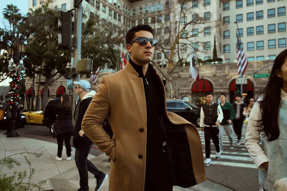 man in brown coat standing on sidewalk during daytime