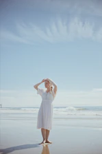 A serene portrait of a woman standing barefoot on a sunlit tropical beach, embodying calm and radiant confidence.