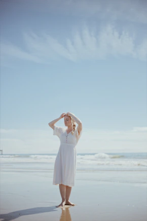 A serene portrait of a woman standing barefoot on a sunlit tropical beach, embodying calm and radiant confidence.