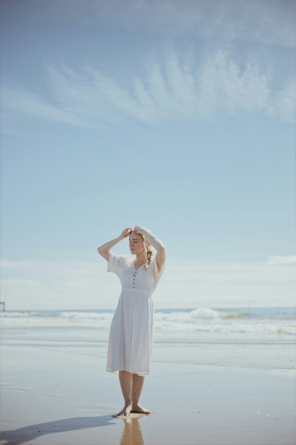 낮 동안 해변에 서 있는 하얀 드레스를 입은 여자