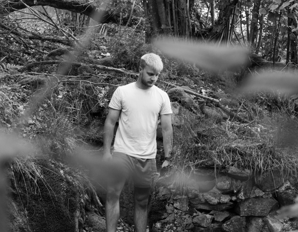 man in white crew neck t-shirt and gray shorts standing on rock in grayscale photography