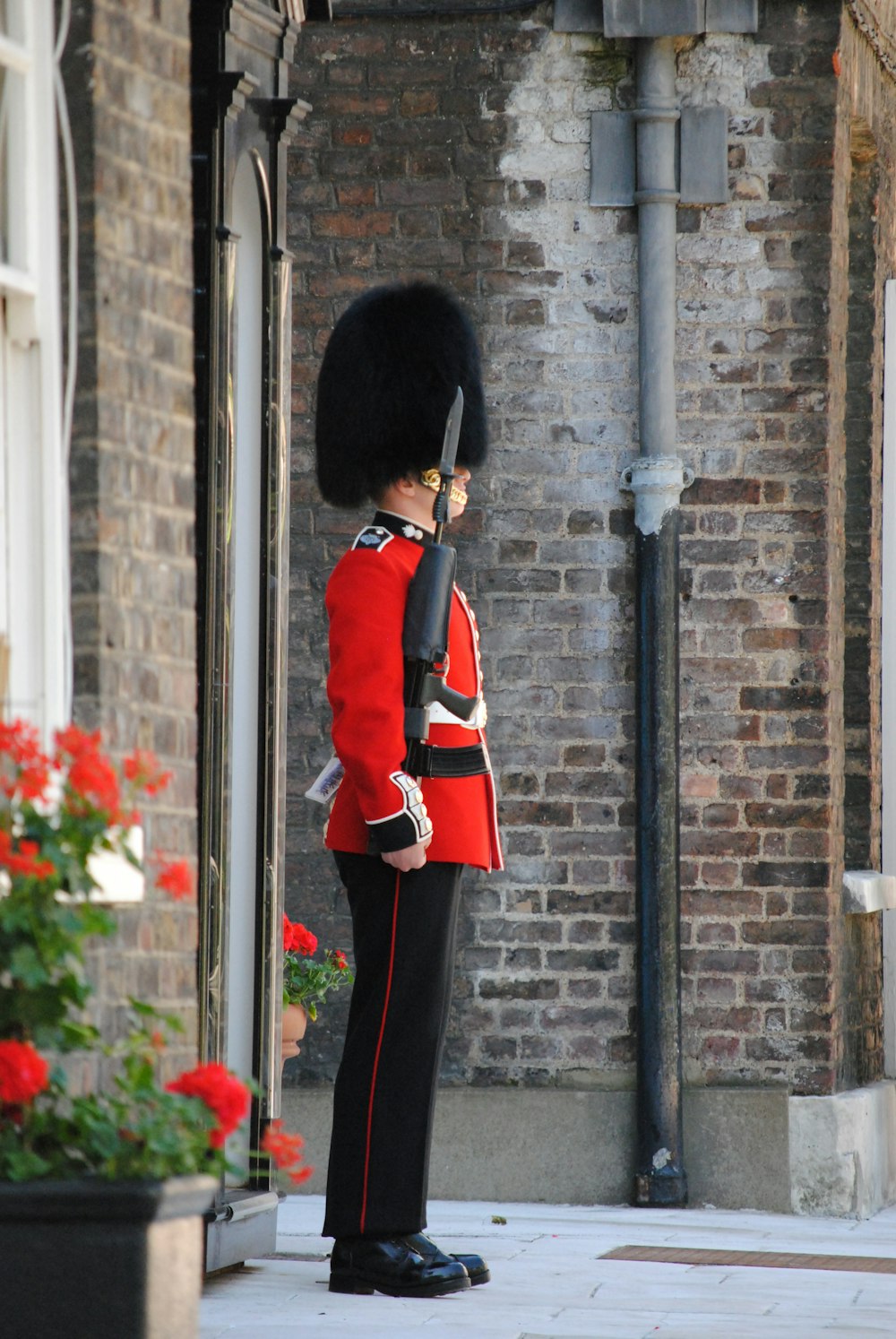 昼間、黒い金属製の支柱のそばに立つ赤と黒の制服を着た人物