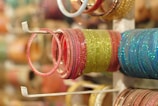 A collection of colorful bangles is neatly arranged on a display stand. The bangles are glittery and vary in colors like pink, green, and blue, with a reflective shine.