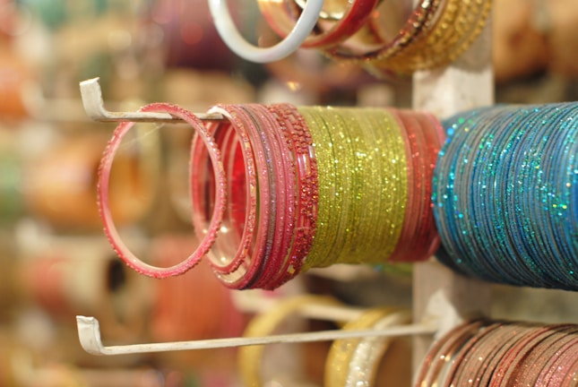A collection of colorful bangles is neatly arranged on a display stand. The bangles are glittery and vary in colors like pink, green, and blue, with a reflective shine.