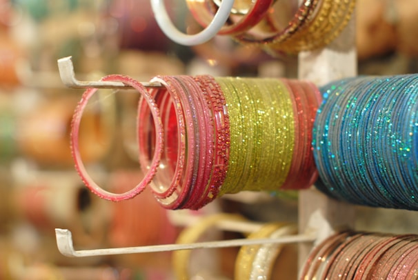 A collection of colorful bangles is neatly arranged on a display stand. The bangles are glittery and vary in colors like pink, green, and blue, with a reflective shine.