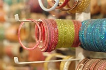 A collection of colorful bangles is neatly arranged on a display stand. The bangles are glittery and vary in colors like pink, green, and blue, with a reflective shine.