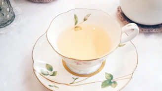 Delicate porcelain tea cups filled with steaming green tea on a light wood tray.