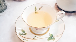 Close-up of a delicate white porcelain cup filled with steaming floral tea, resting on a muted sage linen cloth.