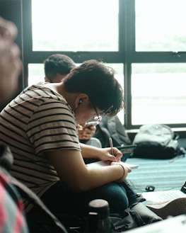 A student happily taking notes during an online tutoring session in a cozy home setting.
