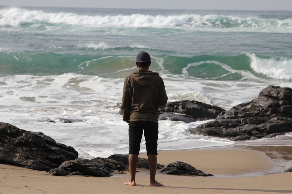 uomo in giacca marrone in piedi in riva al mare durante il giorno