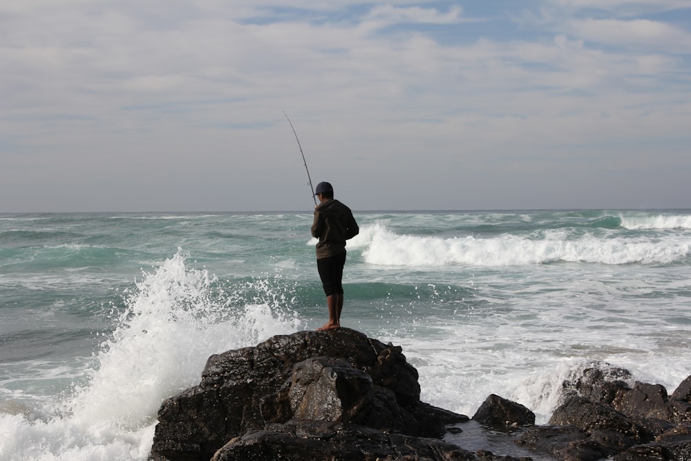 man in black shorts standing on rock near sea during daytime