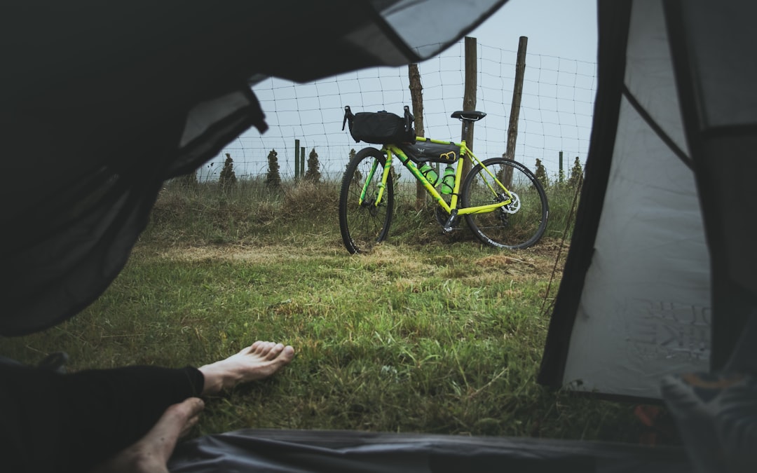 person in black pants sitting on green grass beside green and black mountain bike during daytime