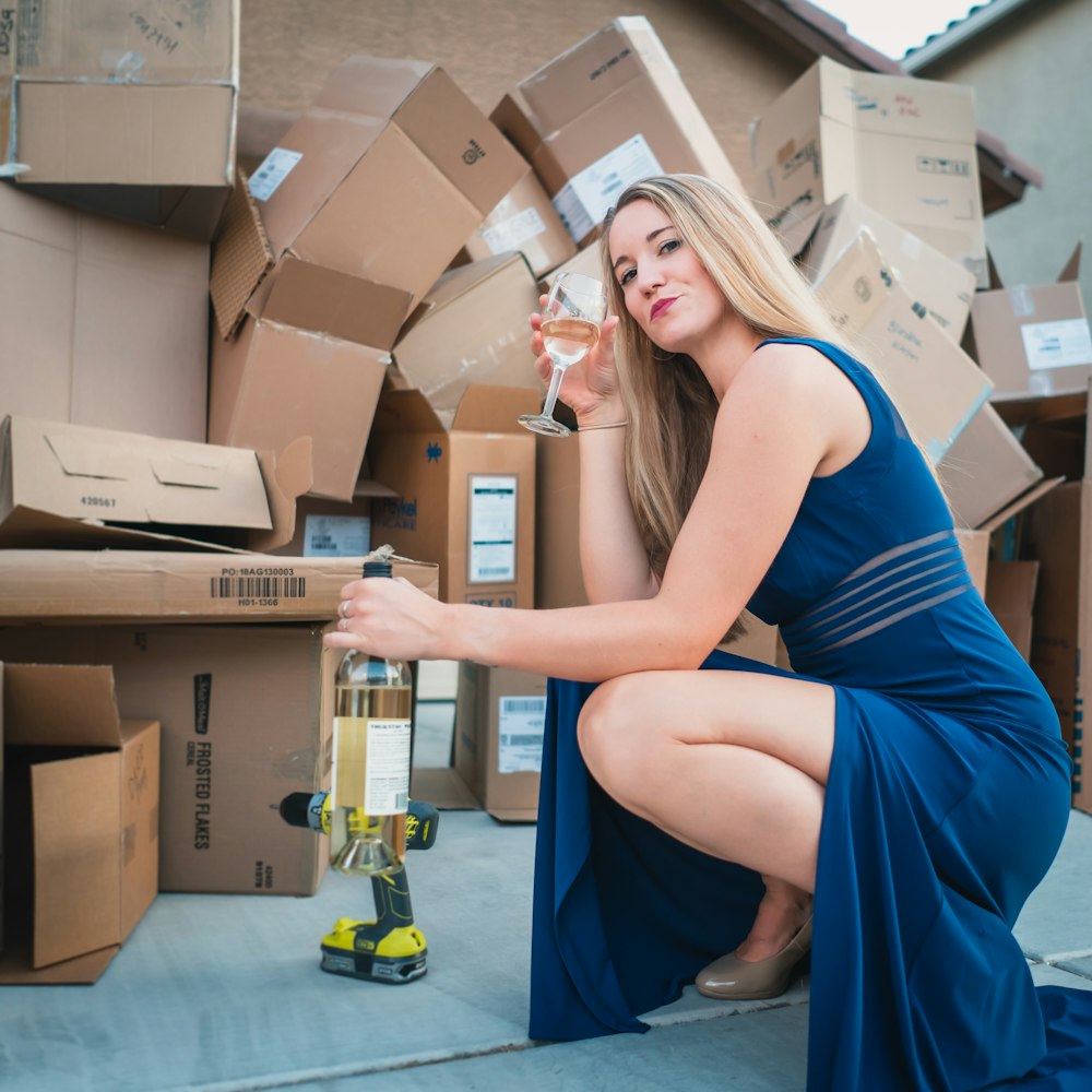 Mujer en vestido azul sin mangas sentada en caja de cartón marrón