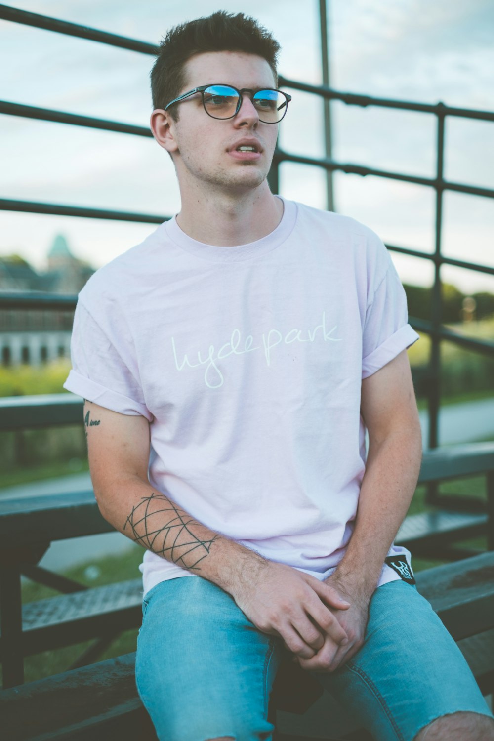 man in white crew neck t-shirt and blue denim shorts sitting on brown wooden bench