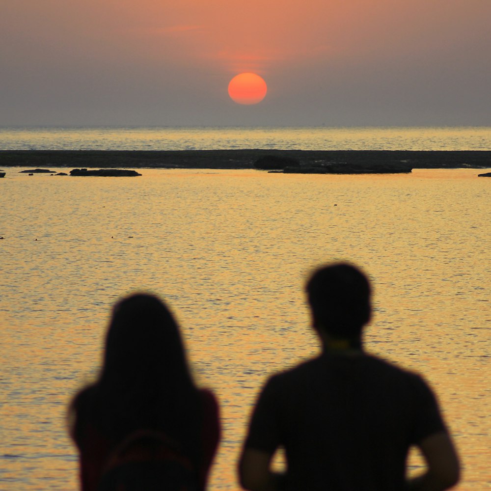 silhouette of 2 person standing on seashore during sunset