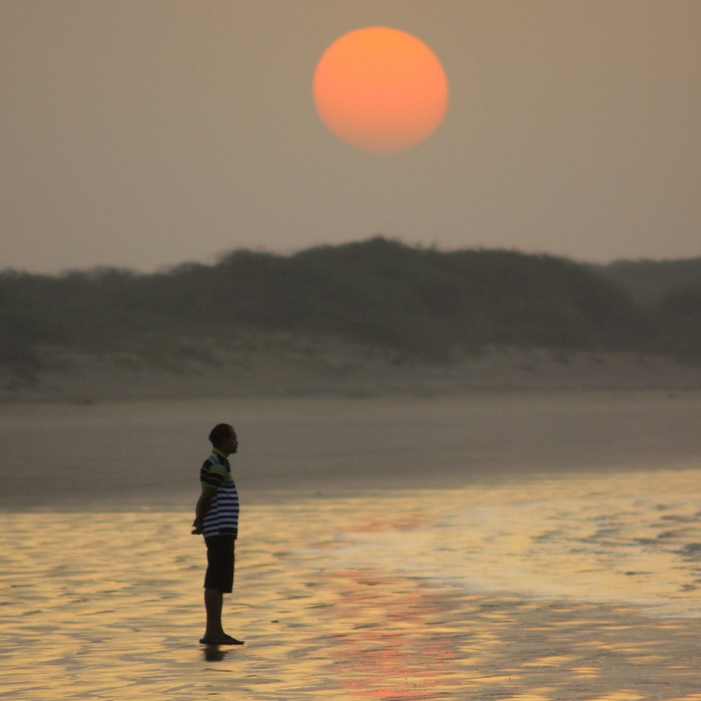 homem na jaqueta preta andando na praia durante o pôr do sol