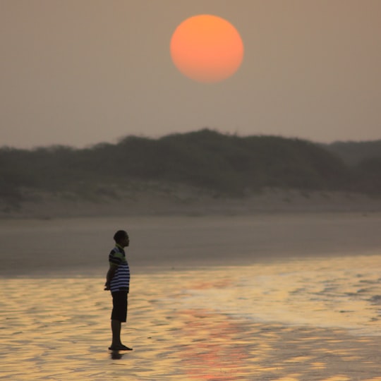 man in black jacket walking on beach during sunset in Diu India