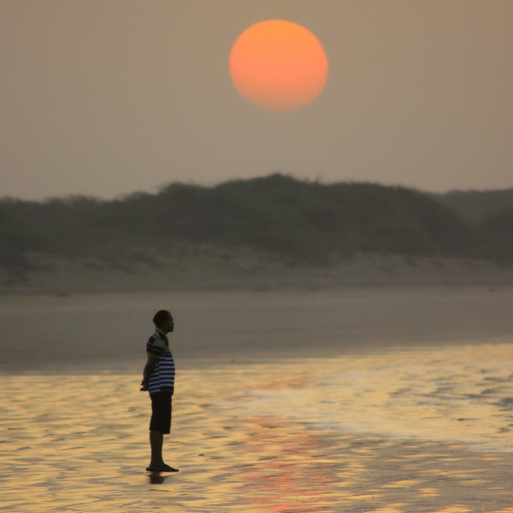 man in black jacket walking on beach during sunset