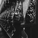 Elegant and intricate wooden carvings line the interior of a structure, displaying detailed floral and geometric patterns. The image captures the play of light and shadow on the ornate designs, enhancing their complexity and craftmanship.