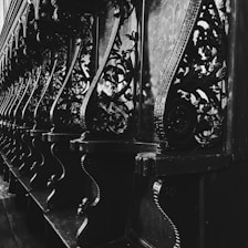 Elegant and intricate wooden carvings line the interior of a structure, displaying detailed floral and geometric patterns. The image captures the play of light and shadow on the ornate designs, enhancing their complexity and craftmanship.