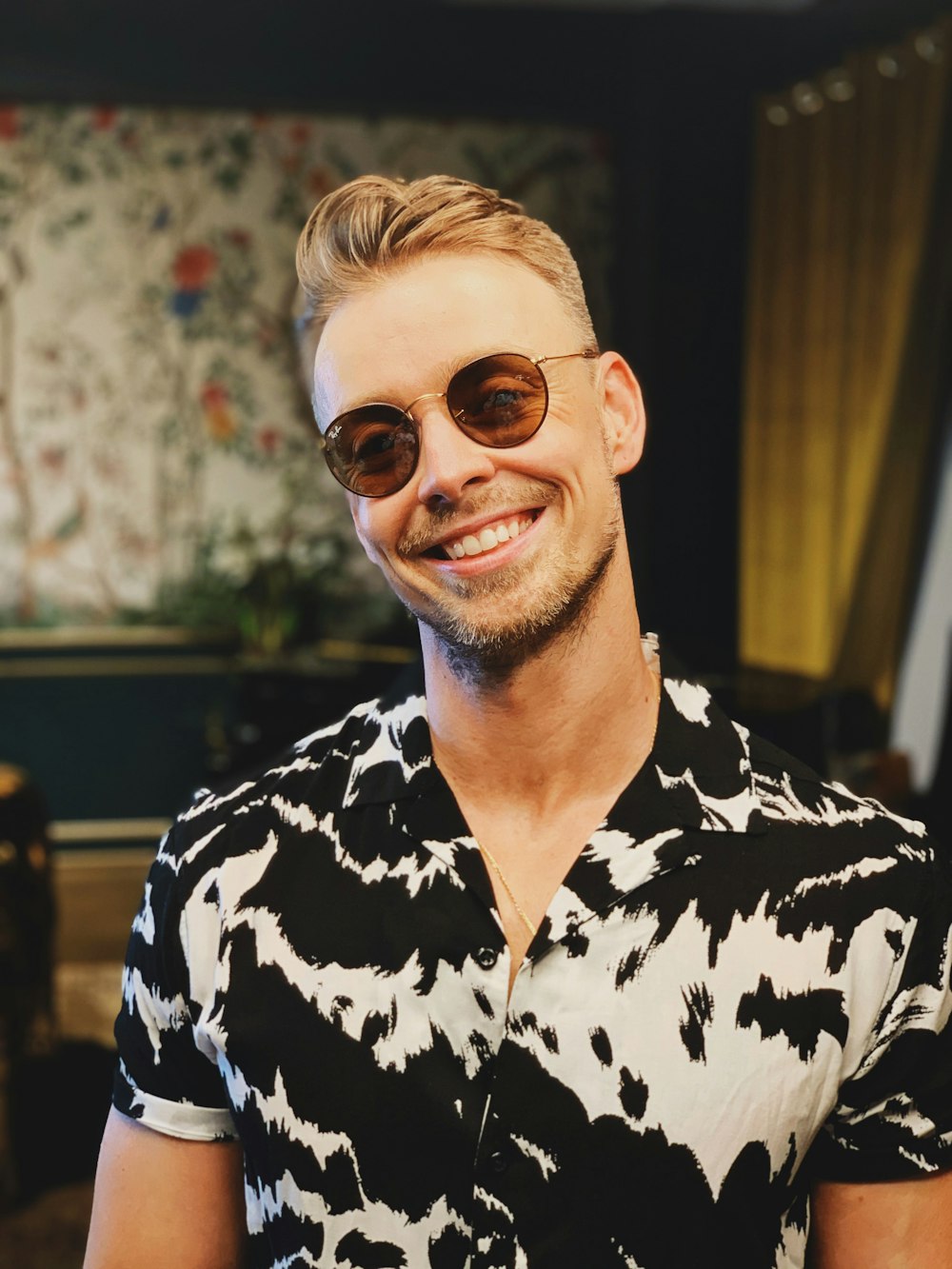 homme en chemise boutonnée à fleurs noire et blanche portant des lunettes de soleil marron