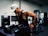 A man wearing a white baseball cap and a black tank top is engaged in a workout at a gym. He has tattoos on his arm and is using gym equipment designed for dips. The background includes more gym equipment and a window, suggesting an indoor gym setting.