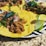 Corn tortillas are topped with shredded meat, chopped red onion, and fresh cilantro, served on a plate with slices of lime. The setting is a granite table surface.