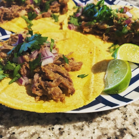 A close-up of tender carnitas served with lime and salsa.