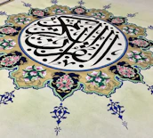 An intricate piece of Islamic art features Arabic calligraphy at its center, surrounded by an ornate floral design. The calligraphy is in bold black lines, creating a striking contrast against a cream background, while the floral elements are rich with details, displaying pink and green hues with blue accents.