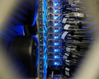 A close-up view of a server rack in a data center, showing rows of servers with blue LED lights glowing. Several network cables are connected to the servers, with labels indicating their connections.