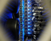 A close-up view of a server rack in a data center, showing rows of servers with blue LED lights glowing. Several network cables are connected to the servers, with labels indicating their connections.