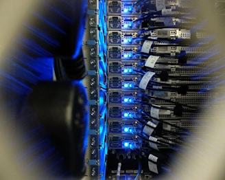 A close-up view of a server rack in a data center, showing rows of servers with blue LED lights glowing. Several network cables are connected to the servers, with labels indicating their connections.