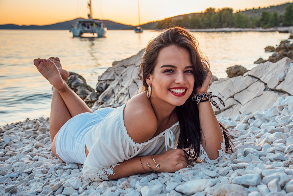 woman in white tank top lying on white textile on beach during daytime