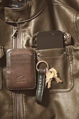A leather jacket with a pocket containing a smartphone and a gray card holder is visible. Attached to the card holder is a key ring holding several keys.
