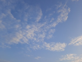 A serene blue sky with soft white clouds drifting gently above a peaceful park bench.