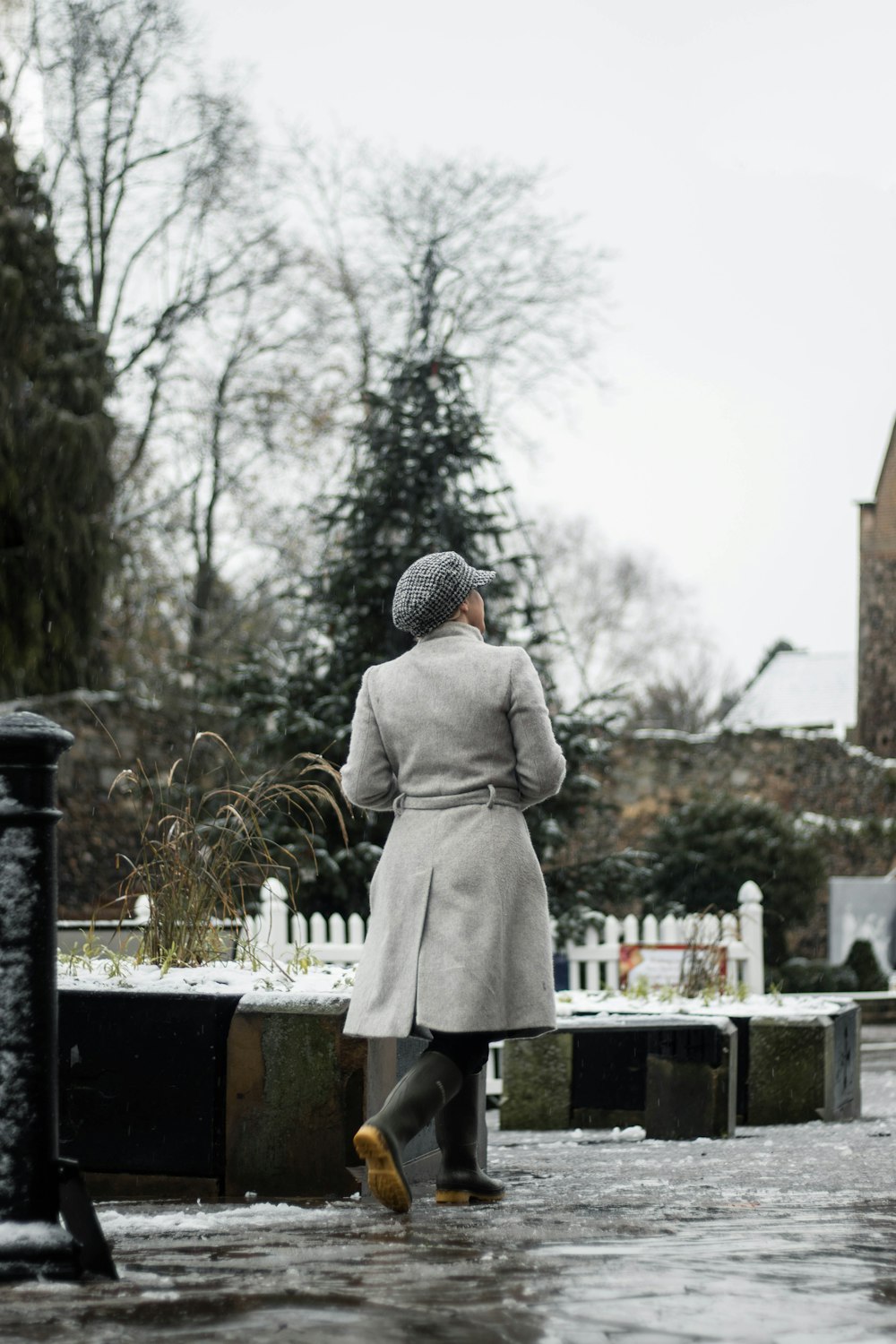 person in gray coat standing near black metal fence during daytime