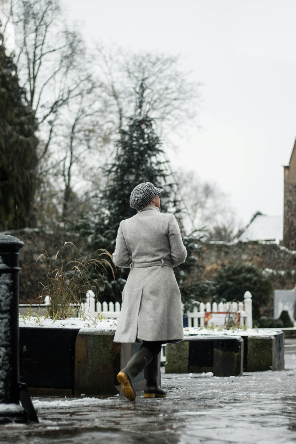 Persona in cappotto grigio in piedi vicino alla recinzione metallica nera durante il giorno