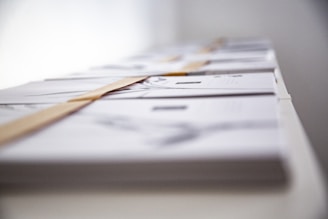 A close-up perspective focused on a line of stacked books or magazines placed horizontally on a surface. The arrangement gives a sense of order and alignment, with each item partially visible and slightly blurred in the background.