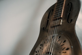 A close-up view of a vintage resonator guitar with metallic body and intricate sound holes, capturing the subtle play of light and shadows on its surface.