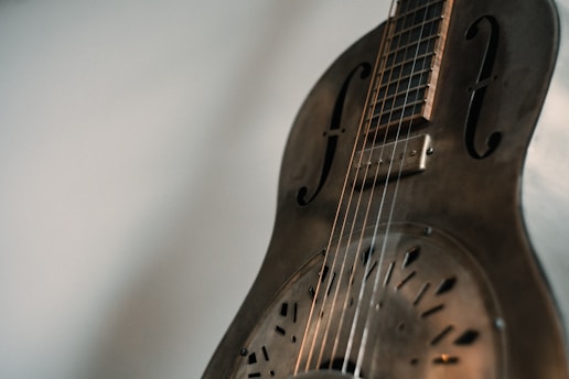 A close-up view of a vintage resonator guitar with metallic body and intricate sound holes, capturing the subtle play of light and shadows on its surface.