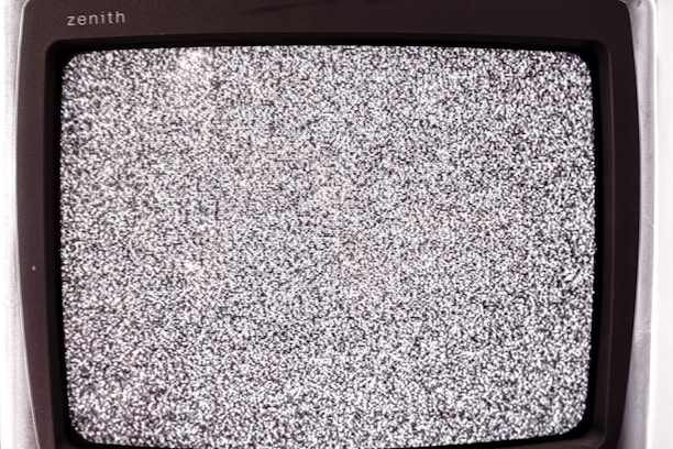 A close-up view of an old television screen displaying static noise. The screen is filled with a pattern of black and white dots and spots, typical of a signal loss or disturbance. The television set has a vintage design with a black frame.