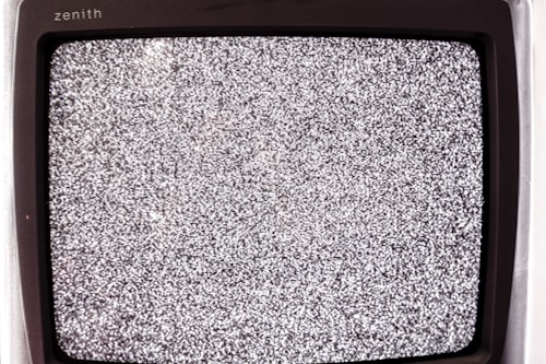A close-up view of an old television screen displaying static noise. The screen is filled with a pattern of black and white dots and spots, typical of a signal loss or disturbance. The television set has a vintage design with a black frame.