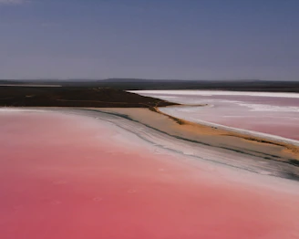 A panoramic view of a red sand dune meeting the clear turquoise waters of a remote Outback lake