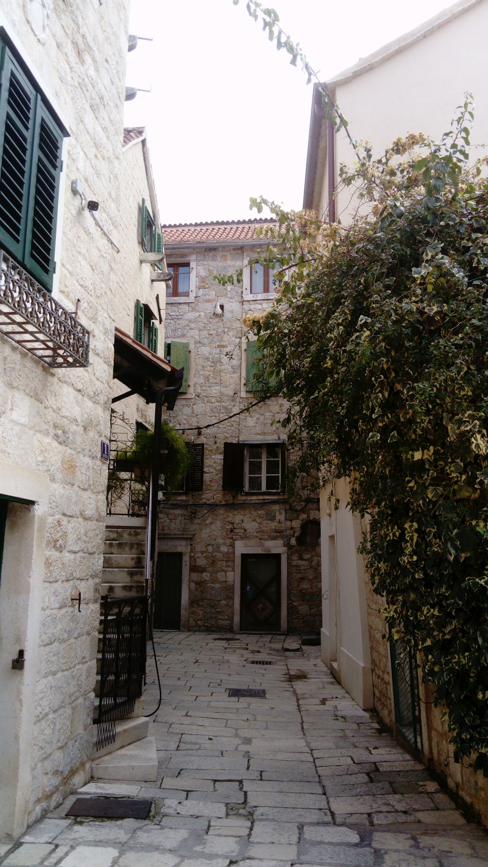 an alley way with a stone building and green shutters