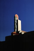 A retro-style theater marquee with the word 'Delta' prominently displayed in vertical letters on a large sign against a deep blue sky. The sign features red, green, and white colors with an art deco design.