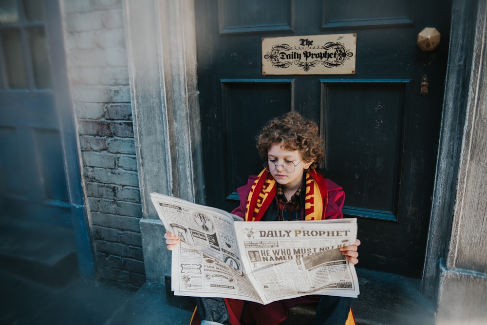 a boy sitting on a step reading a newspaper