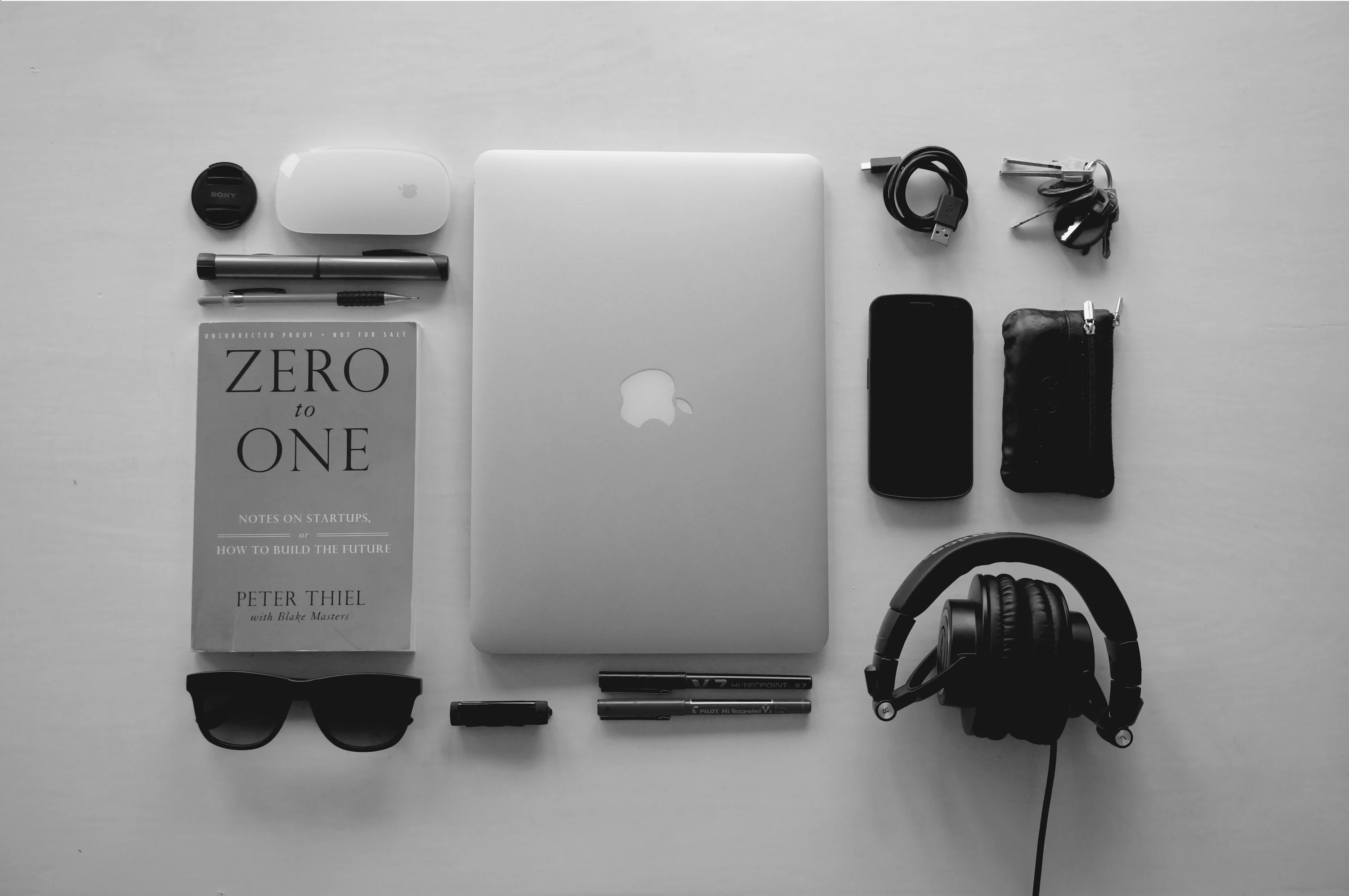 MacBook perak di dekat headphone berkabel hitam dan berbagai macam barang