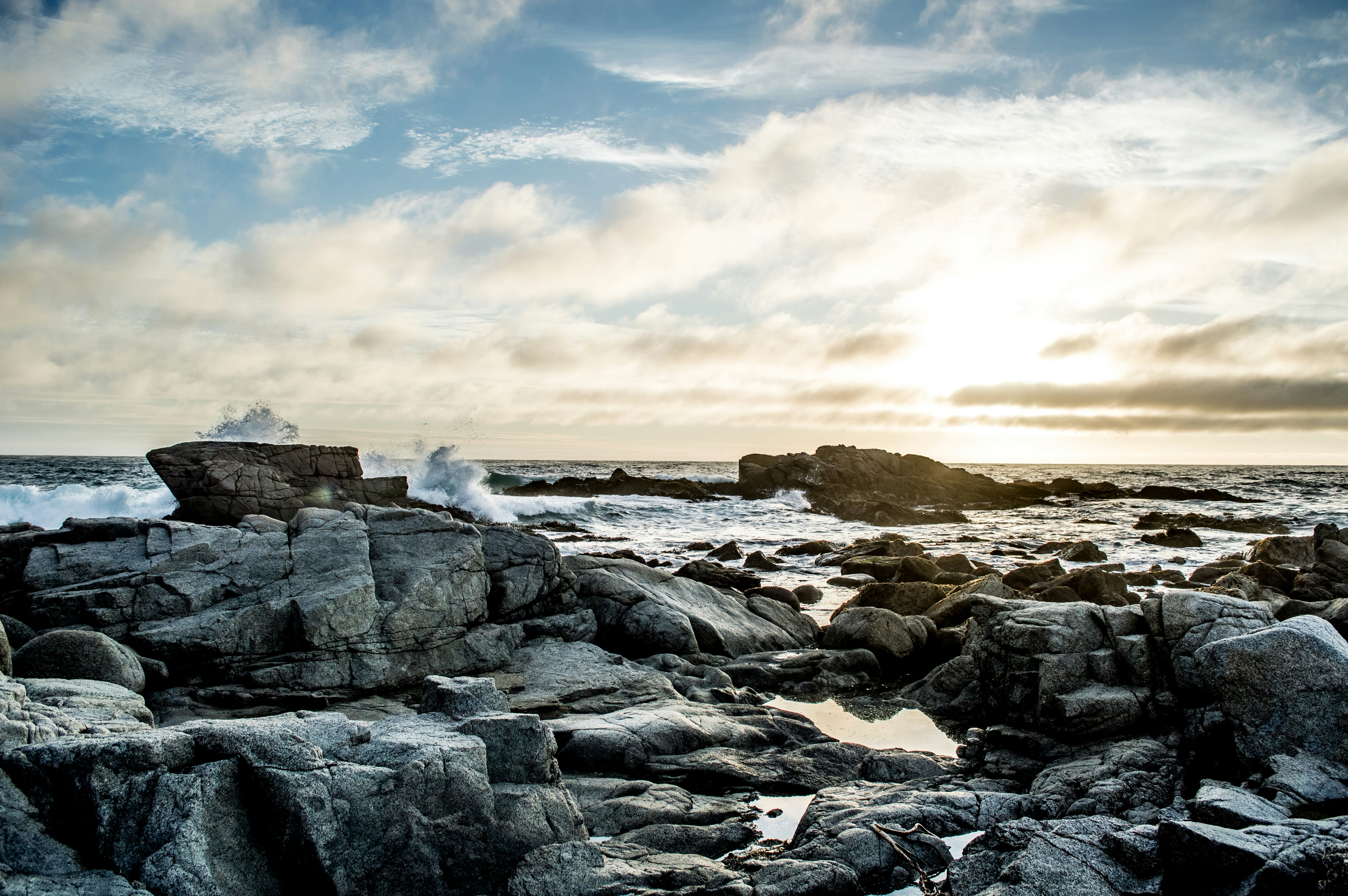 gray concrete rocks on body of water under blue and white cloudy sky