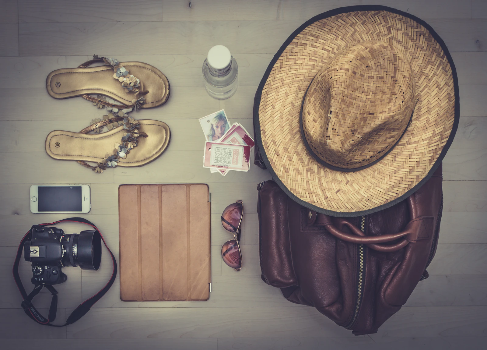 Affaires de voyage disposées à plat : chapeau de paille, sac, appareil photo, sandales et lunettes de soleil